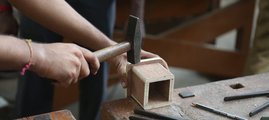 Hammer stroking square wood in the table with pencil on the side